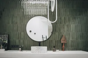 A modern bathroom with green ceramic tiles, a round mirror, and a white vessel sink.