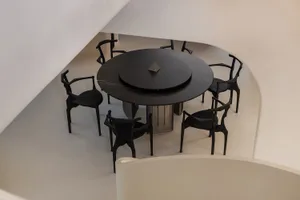 A modern dining room featuring a round black marble table with a central black marble plate, surrounded by black metal chairs