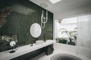 A modern minimalist bathroom featuring green tiles, a round mirror, black faucet, and a round sink.
