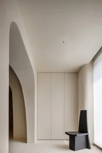 A modern minimalist bedroom with a concrete floor and wall, featuring sleek, clean lines and a unique black chair.
