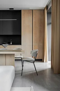 Modern minimalist dining room with wooden cabinets, black accents, and light-colored furniture and curtains.