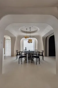 A minimalist dining room with round concrete floor, black chairs, a round table, and abstract lighting fixtures.