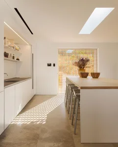 A modern minimalist kitchen with a wooden floor, featuring a long island with stools and a skylight.