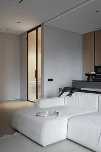 Modern minimalist living room with white fabric sofa, open concept floor plan, and natural light from large windows.