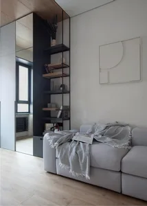 A modern living room with a neutral color palette featuring a large grey sofa, a black shelving unit with books and decoratio