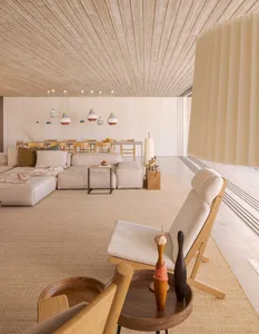 A modern living room featuring neutral-toned furniture, a wooden floor, and a ceiling with linear wood paneling.
