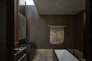 Modern industrial bathroom with dark wood walls, concrete bathtub, and minimalist decor.