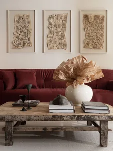 A modern industrial living room with a wooden table, metal sculptures, and paper art on the wall.