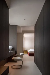 A minimalist bedroom with dark wooden walls and furniture, featuring a white bed and a modern chair.