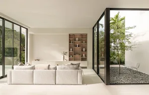 Minimalist living room with a light-colored textile sofa and wooden shelves, glass sliding doors leading to a small garden wi