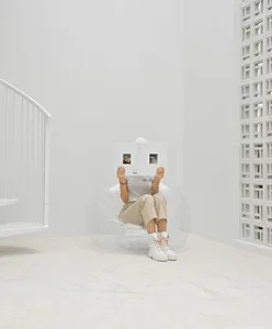 A minimalist room with a clear, inflatable armchair and a person holding a book in their lap.