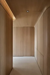 A modern corridor with wooden walls and floors, featuring curved designs and hidden lighting.