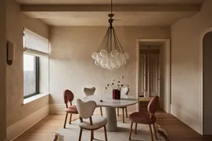 A modern dining room with a marble table, upholstered chairs, and a chandelier with frosted glass globes.