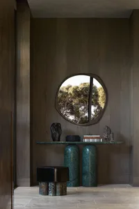A modern interior space featuring a console table with a green marble base and a small round mirrored wall decoration.