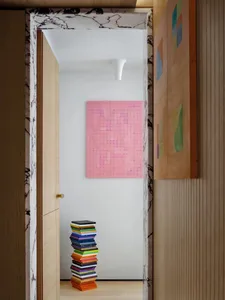 A modern interior hallway with a pink mosaic art piece and a stack of colorful books.