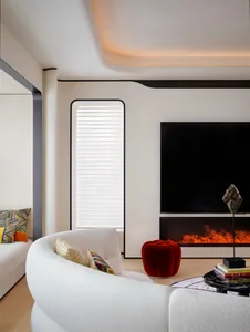 A modern living room featuring concrete walls and floor, with white curvilinear furniture, a red pouf, and a fireplace.