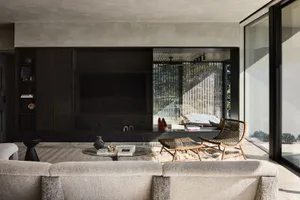 Contemporary living room with concrete walls and glass doors, featuring minimalistic furniture and a cozy atmosphere.