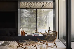 A modern living room with a wooden chair and ottoman, glass shelves, and a leather footstool.