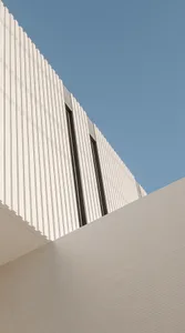 A white, modern metal building with a curved roof and vertical lines against a clear blue sky.