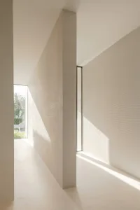 Modern minimalist interior featuring concrete walls and floors, with sunlight filtering through the windows.