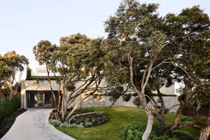 A modern residential exterior featuring concrete walls and lush green trees.