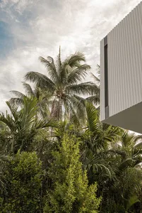 White corrugated metal exterior of a contemporary building, featuring extensive greenery and palm trees.