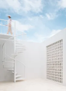 A white architectural space with a spiral staircase and a person walking on the upper floor.