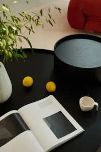 An elegant coffee table setup featuring a black tray, a white cup, lemons, an open magazine, and a green plant.