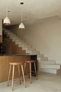 Modern minimalist residential interior featuring a concrete staircase, wooden stools, and pendant lights.