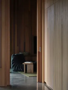 A minimalist interior with wooden paneling, a black pouf chair, and a wooden side table.