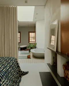 Minimalist bedroom with white concrete walls, floors, and bathtub, featuring a large skylight and a patterned bedspread.