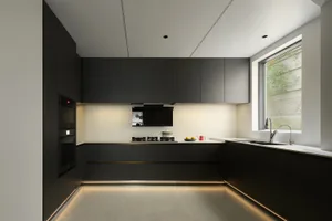 Minimalist kitchen with black cabinets, integrated appliances, and LED lighting beneath the cabinets and along the floor.