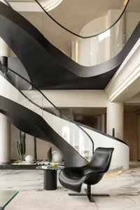 A modern office lounge with a black and white marble floor, metal floating stairs, and a black lounge chair.