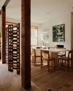 A modern minimalist dining room featuring a wooden table with metal legs, surrounded by wooden chairs, and a large painting o