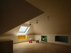 A modern minimalist living room with wooden flooring, featuring a skylight and a built-in bookshelf.