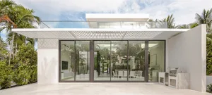 Modern outdoor kitchen with concrete patio and white accents, featuring a grill and seating area with hanging fan.