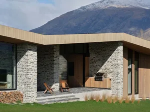 A modern residential building with a stone exterior, featuring a grill and patio area.