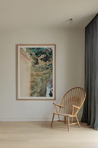 A minimalist living room featuring a wooden armchair and a framed abstract beachscape on the wall.