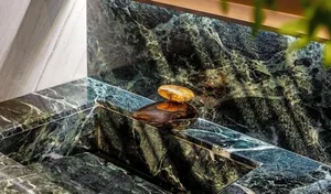 Close-up of a modern bathroom showcasing glossy marble tiles with intricate green veins, featuring a sleek, oval-shaped fauce