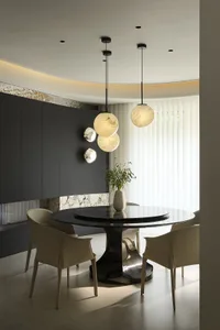 A modern dining room featuring a round black marble table and chairs, illuminated by spherical pendant lights.