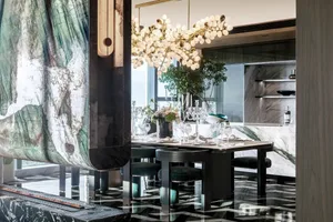 A modern dining room featuring a marble table and floor. Decorative elements include a floral centerpiece and a chandelier.
