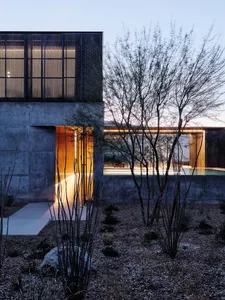 A modern house with a concrete exterior featuring large windows and a swimming pool at dusk.