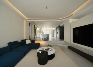 A modern living room with cushions on a blue sofa, a round coffee table, and a large flat-screen TV.