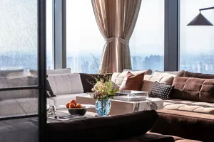 A modern living room featuring textured curtains, a large sectional sofa, and a coffee table with fruits and a vase of flower