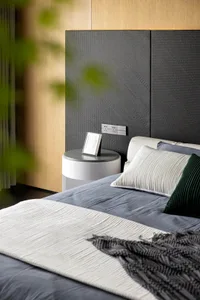 Modern minimalist bedroom featuring a textured headboard, grey blanket, green and white pillows, and grey bedframe with dark