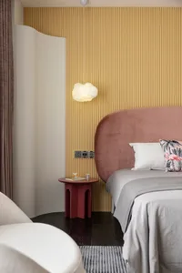 A minimalist bedroom featuring a textured wooden wall, upholstered pink headboard, and a hanging cloud-shaped lamp.