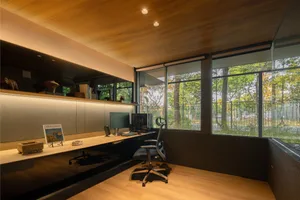A minimalist office space featuring a desk, chair, and computer in a natural setting with large windows.