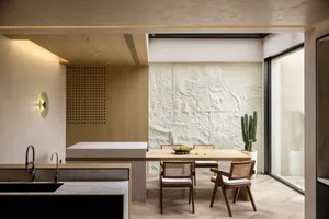 A modern residential kitchen with a sleek white marble countertop, wooden dining table, and cactus plant.