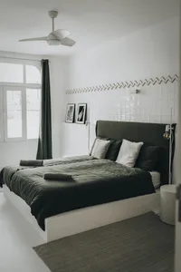Modern, minimalist bedroom with a white bed frame, upholstered headboard, green bedding, and white tile walls