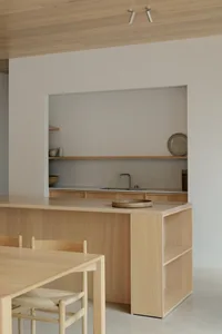 Minimalist kitchen with wooden island and shelves, featuring a concrete backsplash and a kitchen sink.
